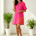 Woman wearing a pink dress with orange hexagon applique in a bright room with plants.
